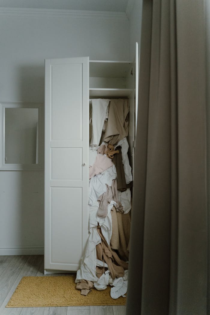 A cluttered wardrobe overflowing with various clothes in a dimly lit room.